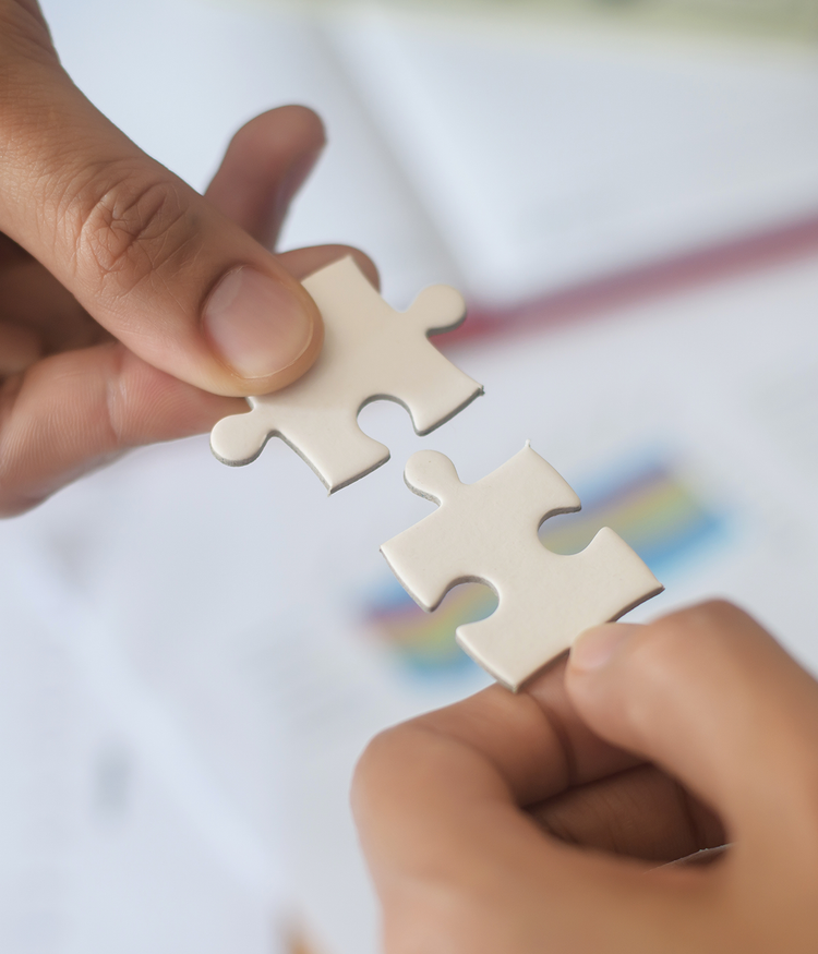 Two hands connecting puzzle pieces on a white surface symbolizing partnership